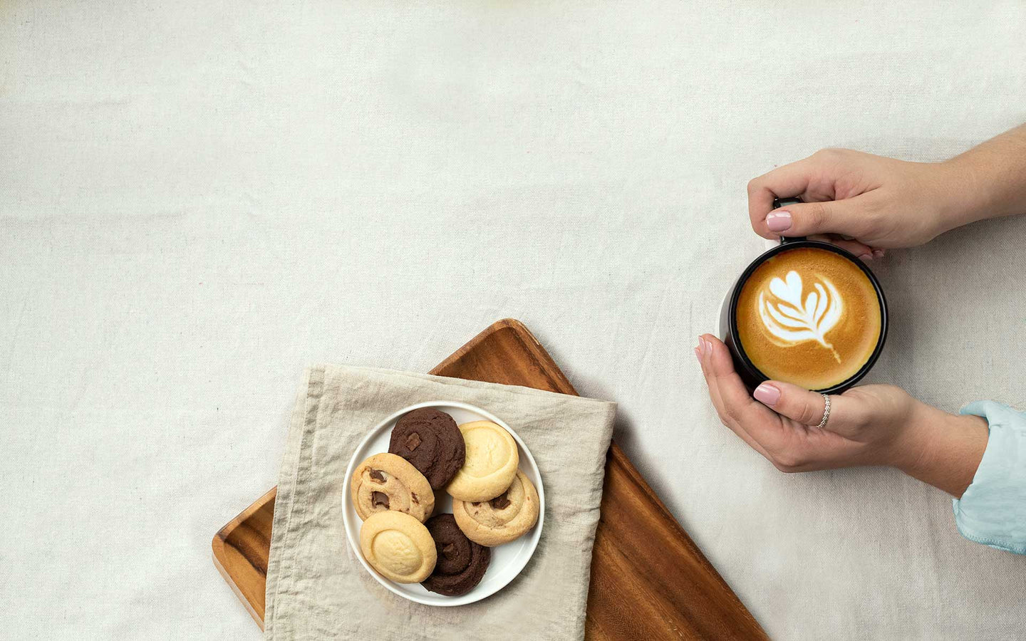 Plate of assorted artisan shortbread cookies with hands holding decorative coffee